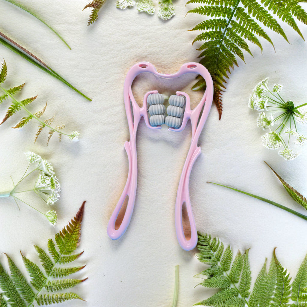 Pink facial roller with small balls surrounded by green leaves and flowers on a light background