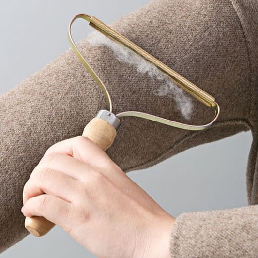 A person using a lint remover with a wooden handle on a beige fabric, with lint being removed visible on the fabric.