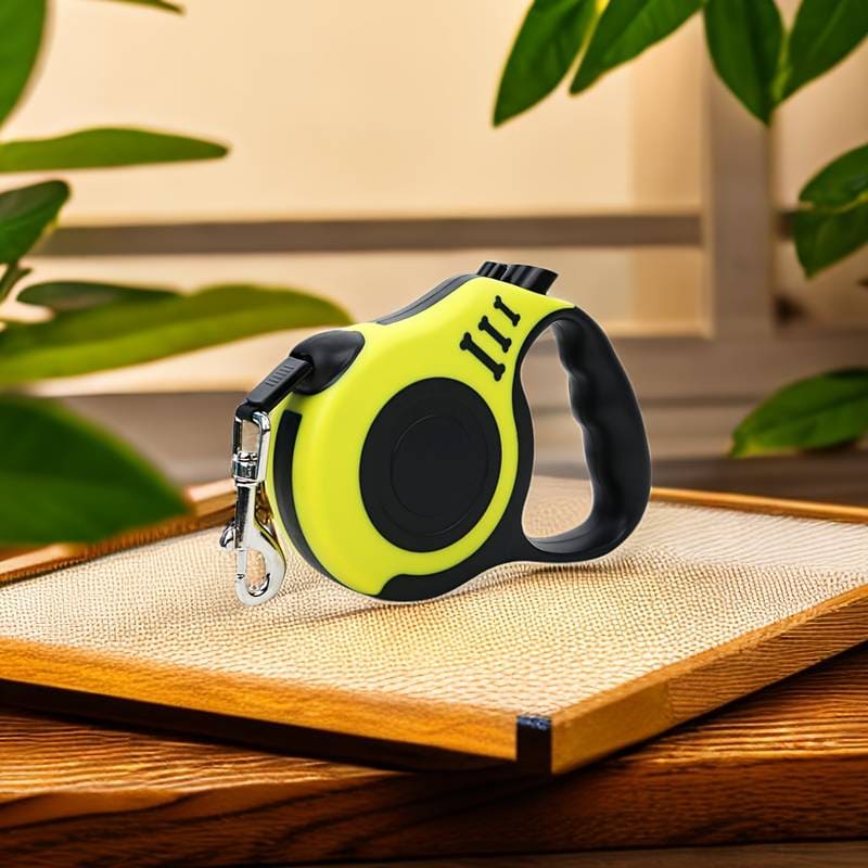 A retractable green and black pet leash with a lock and unlock button, placed on a wooden surface with plants in the background.